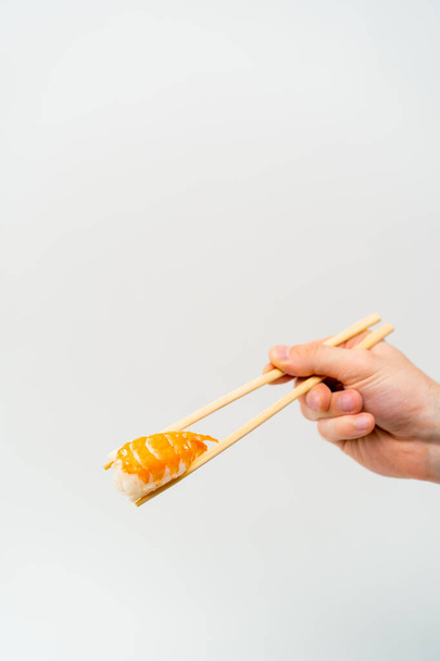 Nahaufnahme der Hand eines Mannes mit Essstäbchen, die Shrimp Sushi in der Luft halten, auf weißem Hintergrund - Foto, Bild