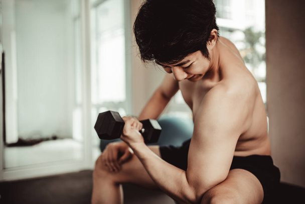 Muskelkräftiger junger Mann trainiert mit Kurzhanteln im Fitnessstudio - Krafttraining und Fitnesskonzept, aktives Gym-Workout, Fitness und Entschlossenheit. - Foto, Bild