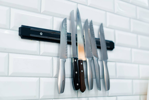 Ένα κοντινό πλάνο ενός σετ μαχαιριών που κρέμονται στον τοίχο στην επαγγελματική κουζίνα του εστιατορίου σούσι - Φωτογραφία, εικόνα
