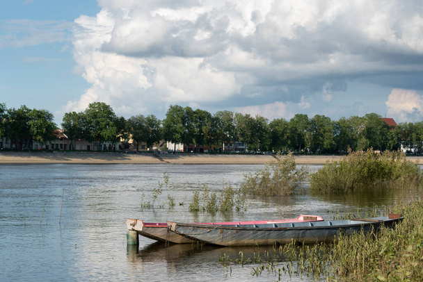 Moored boats in Sava river against city of Slavonski brod and big bright cloud in sky - Foto, Imagen