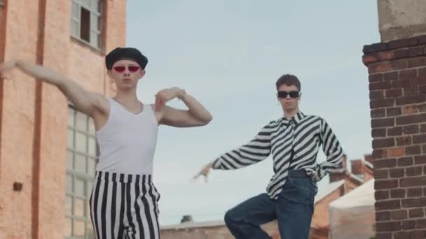 Zwei stylische kaukasische Jungs in schicken Outfits, die draußen vor der Kamera vogulieren - Filmmaterial, Video