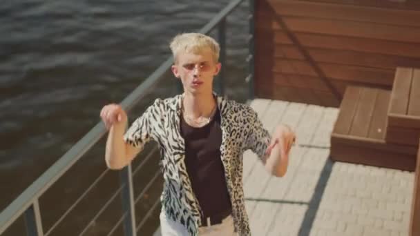Van boven shot van fancy vrouwelijke blonde jongen in dier gedrukt shirt en roze bril dansen mode op jacht in de zomer - Video