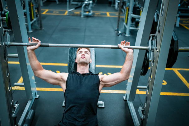Athlète masculin faisant de l'exercice dans la salle de gym, soulevant des poids, tirant des articulations. - Photo, image