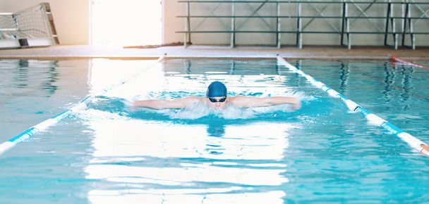 Swimming, sports and man in pool at gym for training, competition and exercise in water. Professional swimmer, fitness and male person practice for challenge, workout and performance for wellness. - Valokuva, kuva