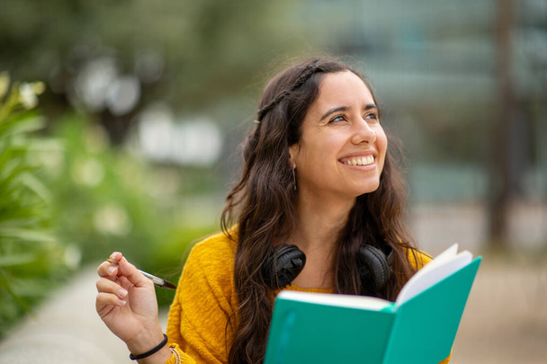 Портрет молодої жінки, яка посміхається з книгою і ручкою - Фото, зображення