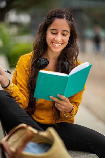Portrait of female student sitting with book and pen - Photo, Image