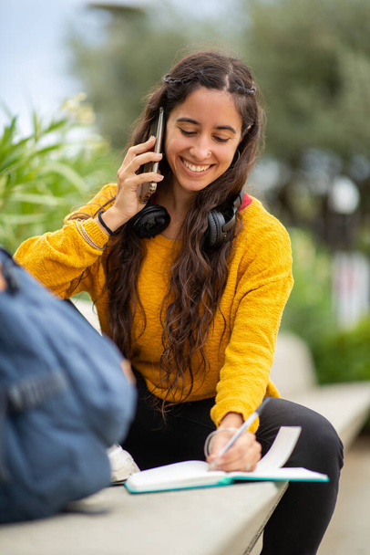 Портрет молодой женщины, разговаривающей с мобильным телефоном и пишущей в книге - Фото, изображение