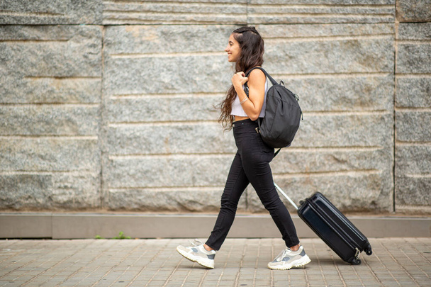 Πλήρες προφίλ σώματος πορτρέτο της νεαρής γυναίκας που περπατά με βαλίτσα - Φωτογραφία, εικόνα