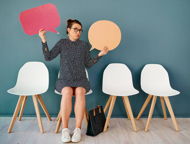 I dont know whos right either. Studio portrait of an attractive young businesswoman holding up speech bubbles while sitting in line against a grey background - Photo, Image