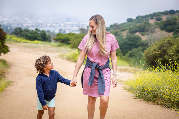 glimlachende moeder hand in hand met zoon tijdens het wandelen in de natuur, familie zorg en reizen concept  - Foto, afbeelding
