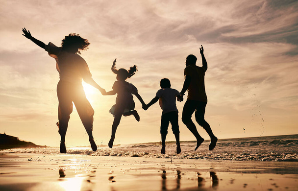 Silhouet, familie springen op het strand en zonsondergang met oceaangolven, achteraanzicht en hechting in de natuur. Energie, mensen die elkaars hand vasthouden in de lucht, buiten en op vakantie, vrijheid en reizen, vertrouwen en liefde in Mexico. - Foto, afbeelding