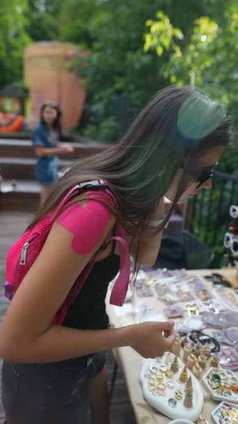 una joven seleccionando una pieza de joyería en la feria. Imágenes FullHD de alta calidad - Metraje, vídeo