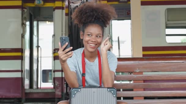 Ázsiai tizenéves lány afro-amerikai utazó okostelefon moblie, miközben várja a vonat egy állomáson. Kiváló minőségű 4k felvételek - Felvétel, videó