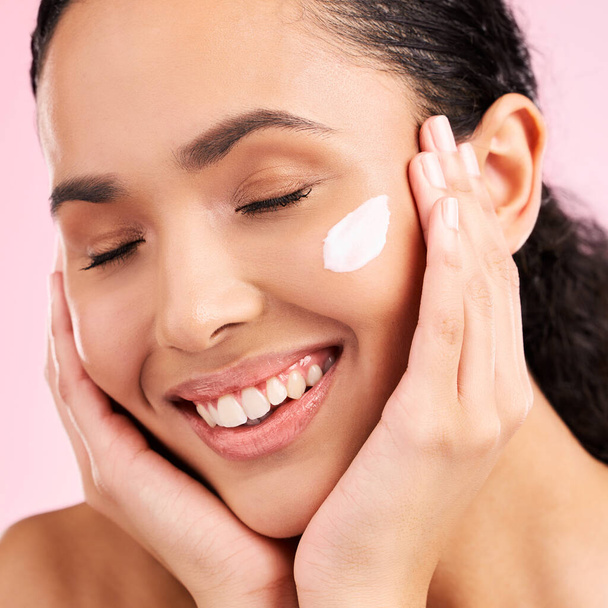 Skincare, happy and woman with face cream in studio isolated on a pink background. Smile, beauty and natural model with moisturizer, cosmetic and apply dermatology product for wellness and health. - Foto, afbeelding