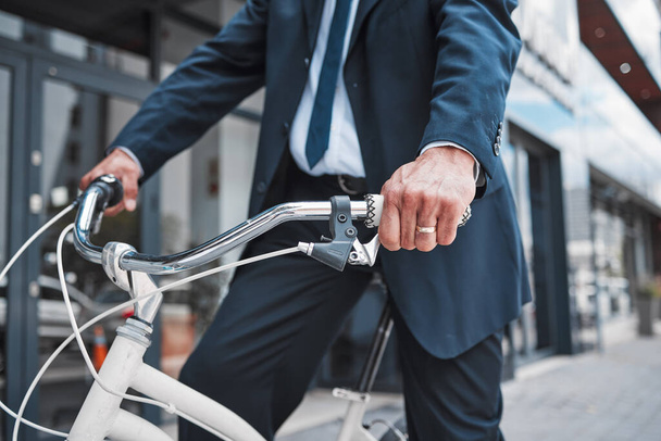 Hands, bicycle and businessman cycling in the city or riding for eco friendly travel, transport or commute to office, building or work. Man, driving and bike for carbon neutral footprint in town. - Photo, Image