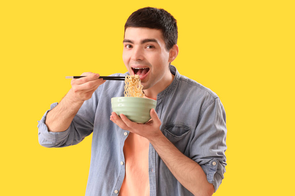 Young man eating Chinese noodles on yellow background - Photo, Image