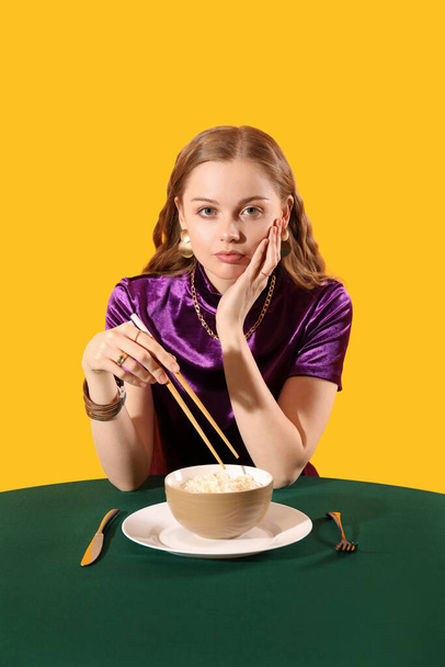 Young woman with bowl of Chinese noodles at table on yellow background - Photo, Image