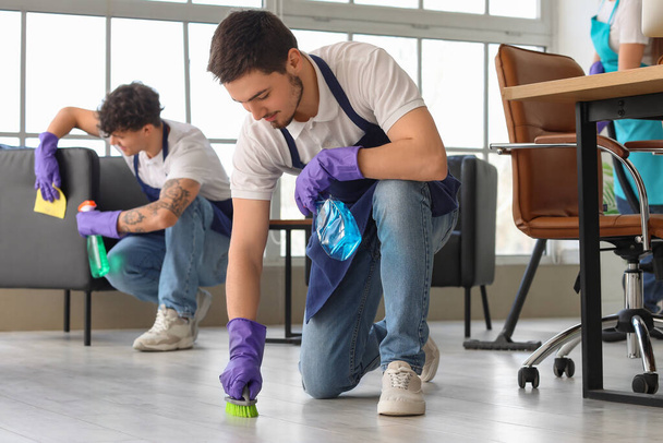 Male janitor cleaning floor with brush in office - Photo, Image