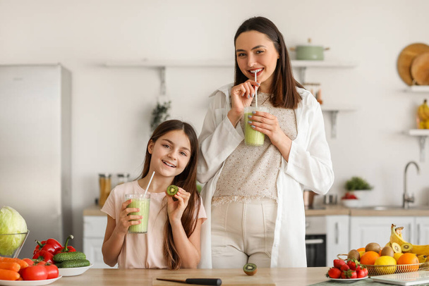 Kleines Mädchen mit schwangerer Mutter trinkt grünen Smoothie in der Küche - Foto, Bild