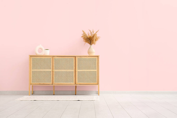 Cómoda moderna con césped de pampas y decoración cerca de la pared rosa en la habitación - Foto, imagen