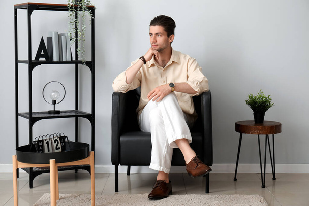 Стильный молодой человек с наручными часами сидит на кресле в комнате - Фото, изображение