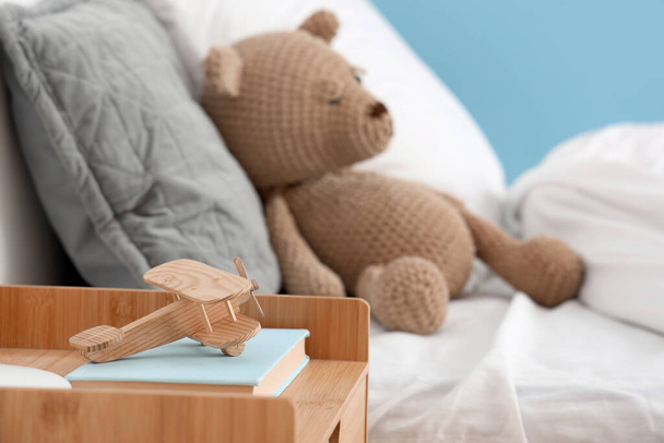 Houten speelgoed vliegtuig en boeken op nachtkastje in kinderslaapkamer, close-up - Foto, afbeelding
