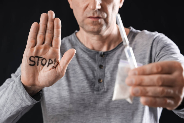 Mature junkie with drugs and word STOP on his palm against black background, closeup - Φωτογραφία, εικόνα