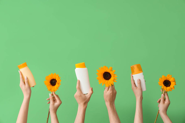 Vrouwelijke handen met flessen zonnebrandcrème en zonnebloemen op groene achtergrond - Foto, afbeelding