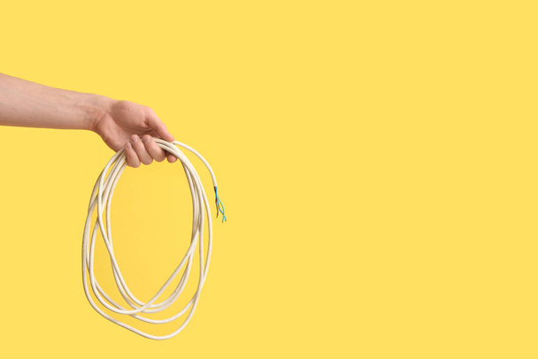 Electrician hand with wire on yellow background - Фото, изображение