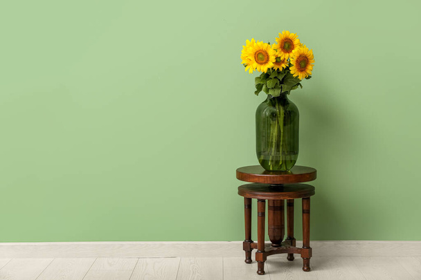 Jarrón con hermosos girasoles en el taburete cerca de la pared verde en la habitación - Foto, imagen