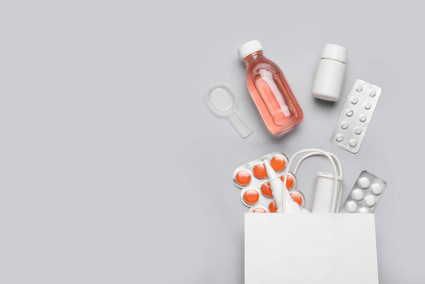 Papieren zak met verschillende pillen en flessen medicijnen op grijze achtergrond - Foto, afbeelding