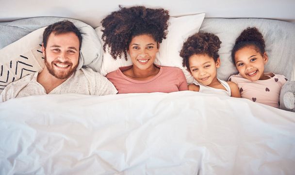 Family, happy and portrait in bed at home for quality time, bonding or morning routine. Above, mixed race and smile of a man, woman and children together in a bedroom with love, care and comfort. - Photo, Image