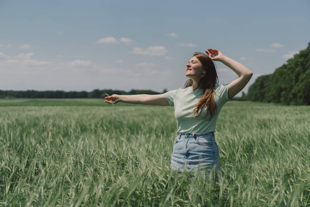 A woman enjoys the fresh air in nature in a green barley field. Summer countryside and gathering flowers. Atmospheric tranquil moment - Fotografie, Obrázek