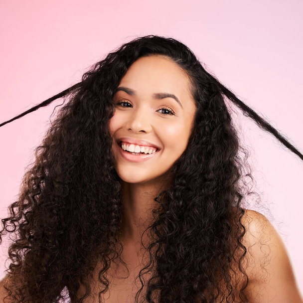 Face, woman and curly hair pull for beauty in studio isolated on a pink background. Portrait, natural cosmetics and hairstyle of happy model in salon treatment for growth, wellness and aesthetic. - 写真・画像