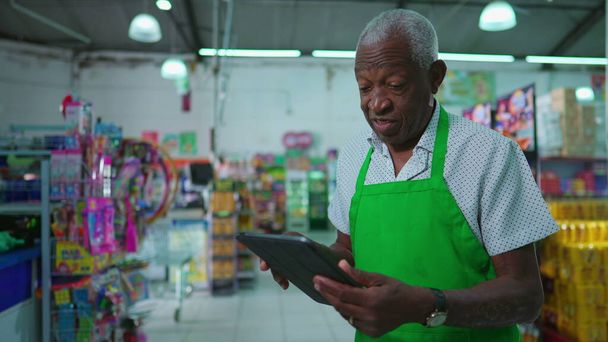 Afroameričtí starší zaměstnanci supermarketu pomocí tabletu zařízení stojící uvnitř obchodu s potravinami, zaměstnání černošské starší osoby na pracovišti, kontrola inventáře - Fotografie, Obrázek