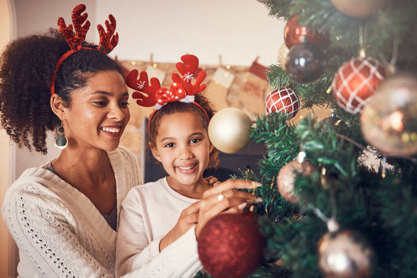 Christmas, portrait and mother with girl decorating tree, bonding and happy together. Xmas, smile and face of kid with African mom with ornament for family party, celebration or holiday event in home. - Photo, Image