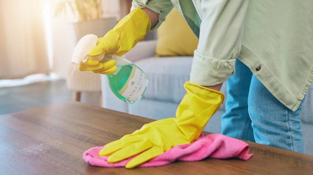 Woman, hands and cleaning table with spray for housekeeping, hygiene or bacteria removal at home. Female person or cleaner spraying chemical bottle for germs, dirt and wiping wooden desk or furniture. - Photo, Image