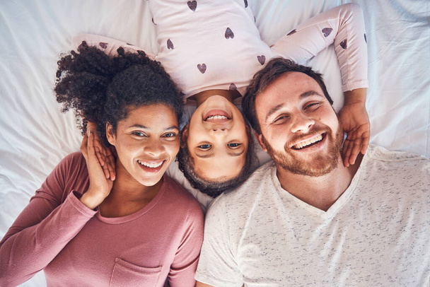 Smile, happy family and portrait on bed at home for quality time, bonding or morning routine. Above, mixed race and face of a man, woman and girl kid together in a bedroom with love, care and comfort. - Photo, Image