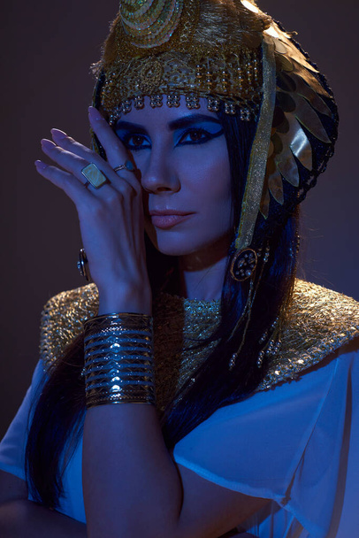 Portrait of beautiful woman in Egyptian headdress posing in blue light on brown background - Photo, Image