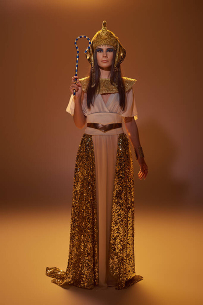 Piena lunghezza di donna elegante in abbigliamento egiziano tenendo truffatore e in piedi su sfondo marrone - Foto, immagini