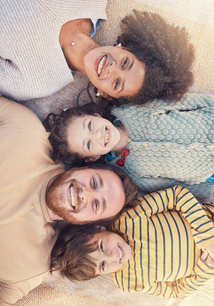 Portrait, happy family and top view on carpet in home for bonding together. Face, smile and parents with children on floor, interracial mother and father with kids, love and care for quality time. - Photo, Image