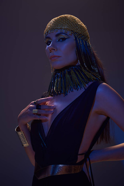 Arckép gyönyörű nő egyiptomi öltözékben pózol, és nézi a kamera barna kék fény - Fotó, kép