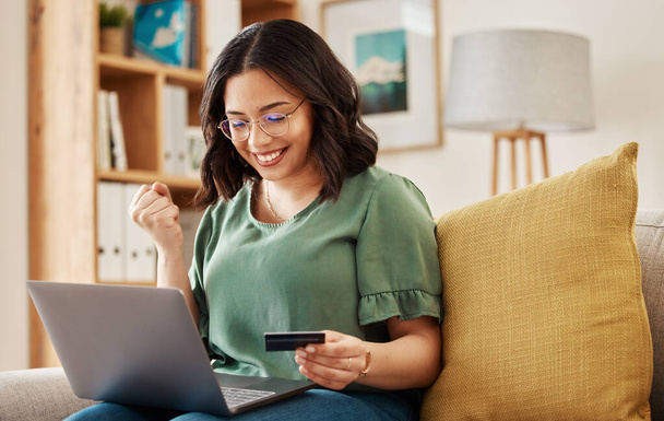 Winning, laptop and credit card, happy woman on sofa in living room for internet banking in home. Ecommerce payment, smile and cashback, girl at computer browsing retail website for online shopping - Photo, Image
