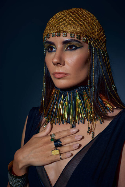 Brunette woman with egyptian makeup and attire posing in headdress on blue background - Foto, imagen