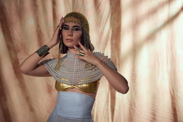 Elegante donna in copricapo egiziano e perla superiore guardando la fotocamera su sfondo astratto - Foto, immagini
