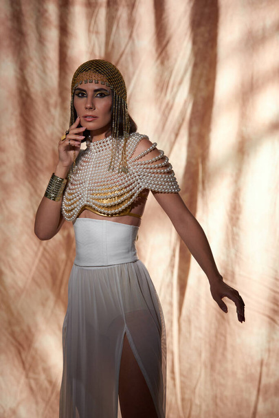 Elegant woman in egyptian headdress and pearl top looking at camera on abstract background - Φωτογραφία, εικόνα