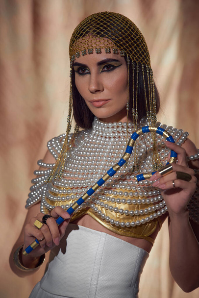 Elegant woman in headdress and pearl top holding egyptian crook on abstract background - Photo, Image