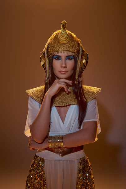 Elegante donna bruna con trucco e abbigliamento egiziano guardando la fotocamera su sfondo marrone - Foto, immagini