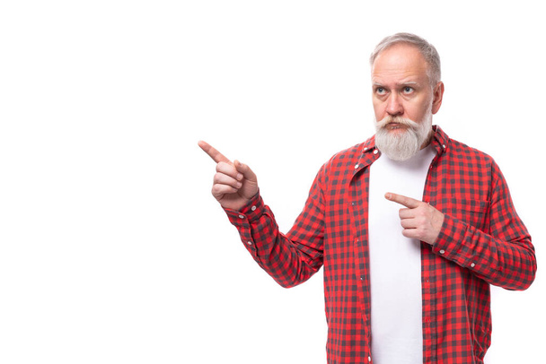 Ältere gutaussehende grauhaarige Mann mit einem Bart zeigt einen Finger zur Seite auf einem weißen Hintergrund. - Foto, Bild