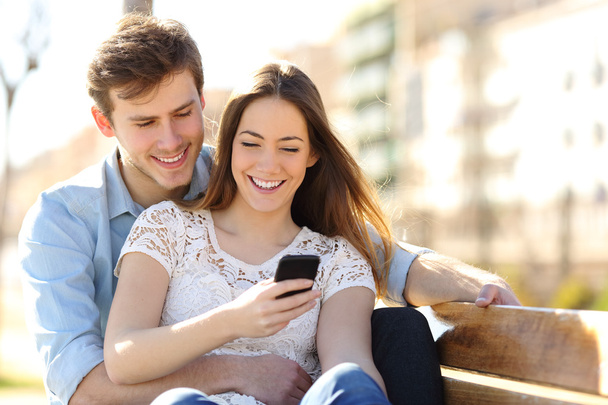 Couple sharing media in a smart phone in a park - Foto, Imagem